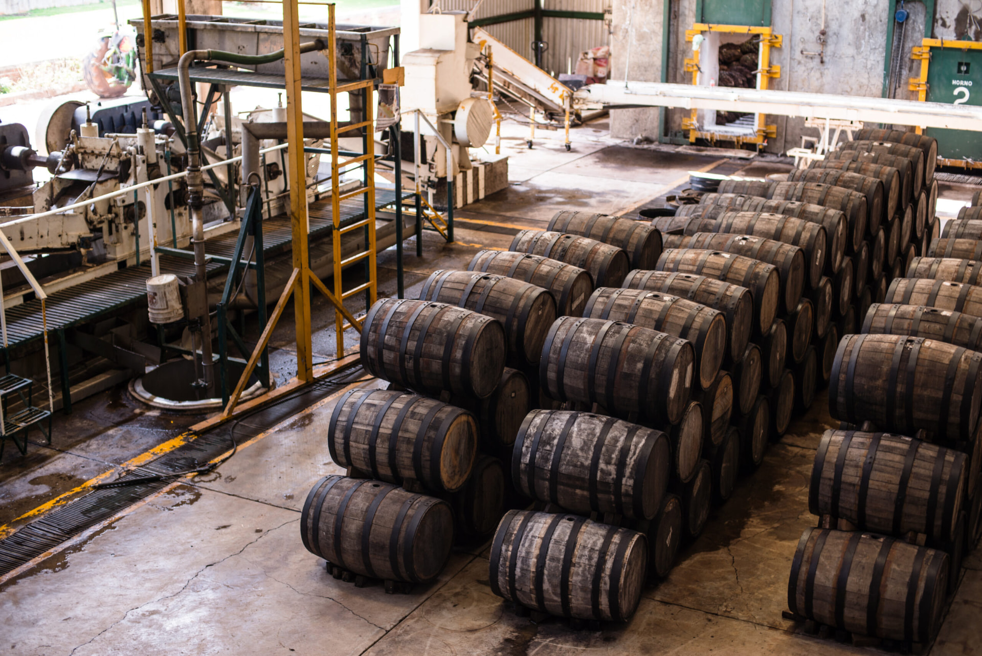 Rows of stacked barrels beside production equipment and the agave ovens at NOM 1414 in Arandas, Jalisco