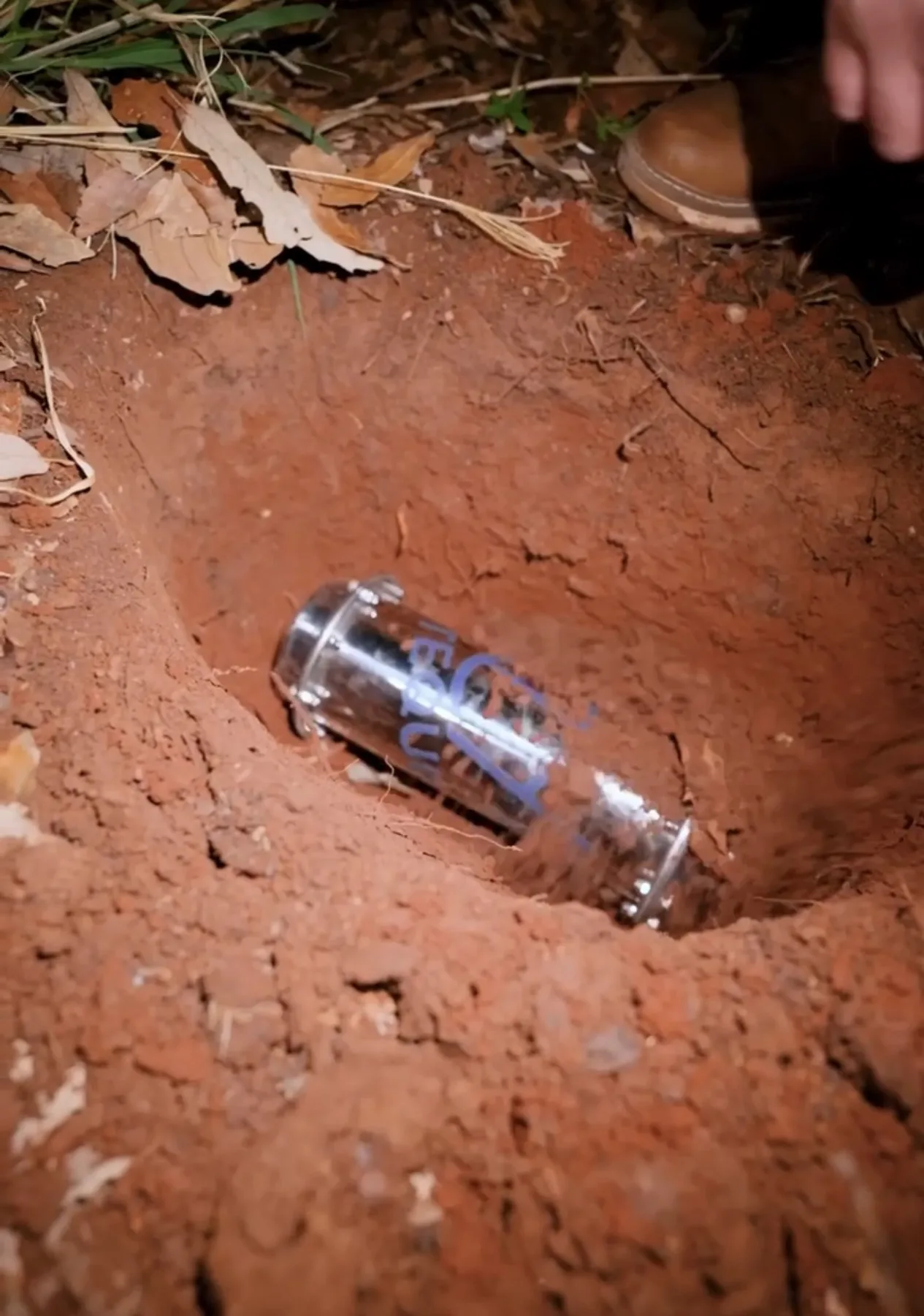 A Yéyo bottle lying in the bottom of the hole as red soil falls over it
