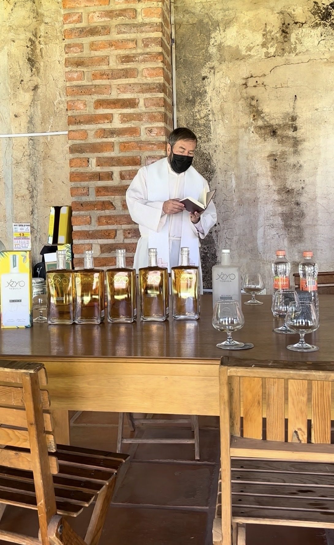 A priest reading a blessing behind a table of Yéyo bottles and glasses at the distillery